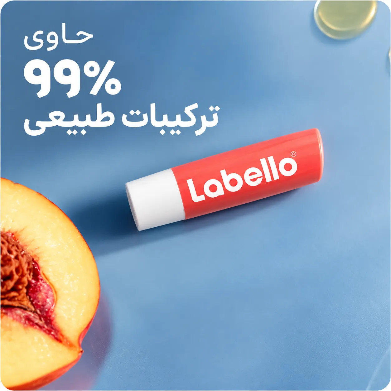 تیوپ بالم لب هلویی لبلو با درپوش سفید روی پس‌زمینه آبی، کنار نصفه هلو
